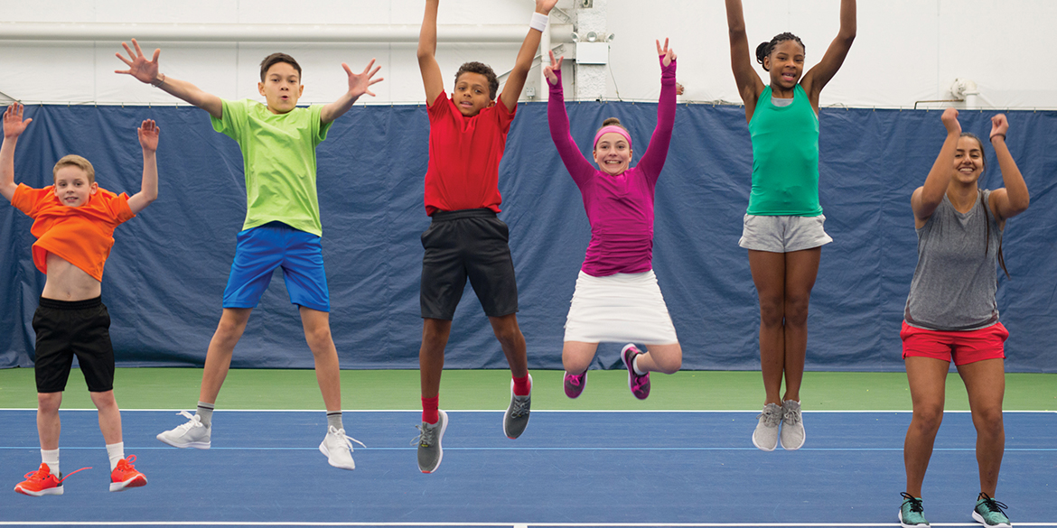 Young athletes jumping in the air with their coach.