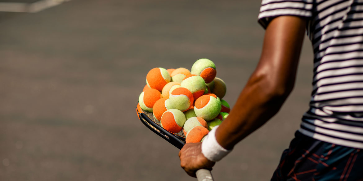 A kid balances tennis balls on his racquet.
