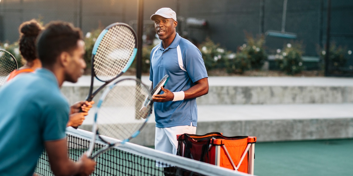 Tennis coach on a court with two students facing the net