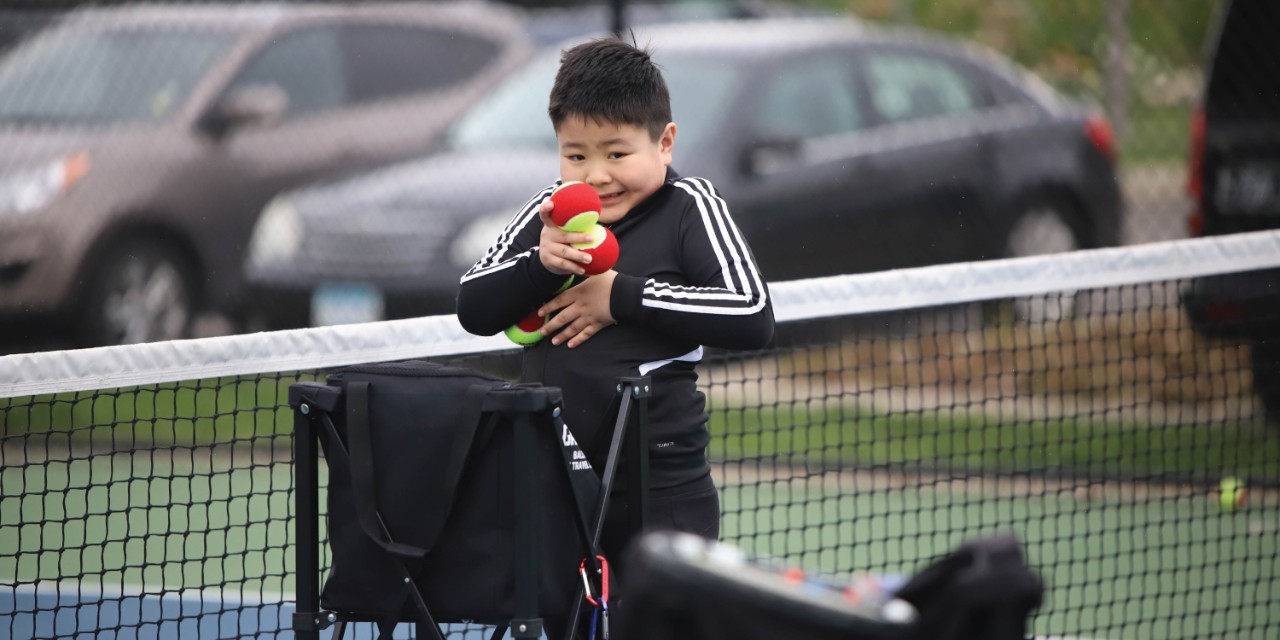 Young boy holding tennis balls on the court near the net
