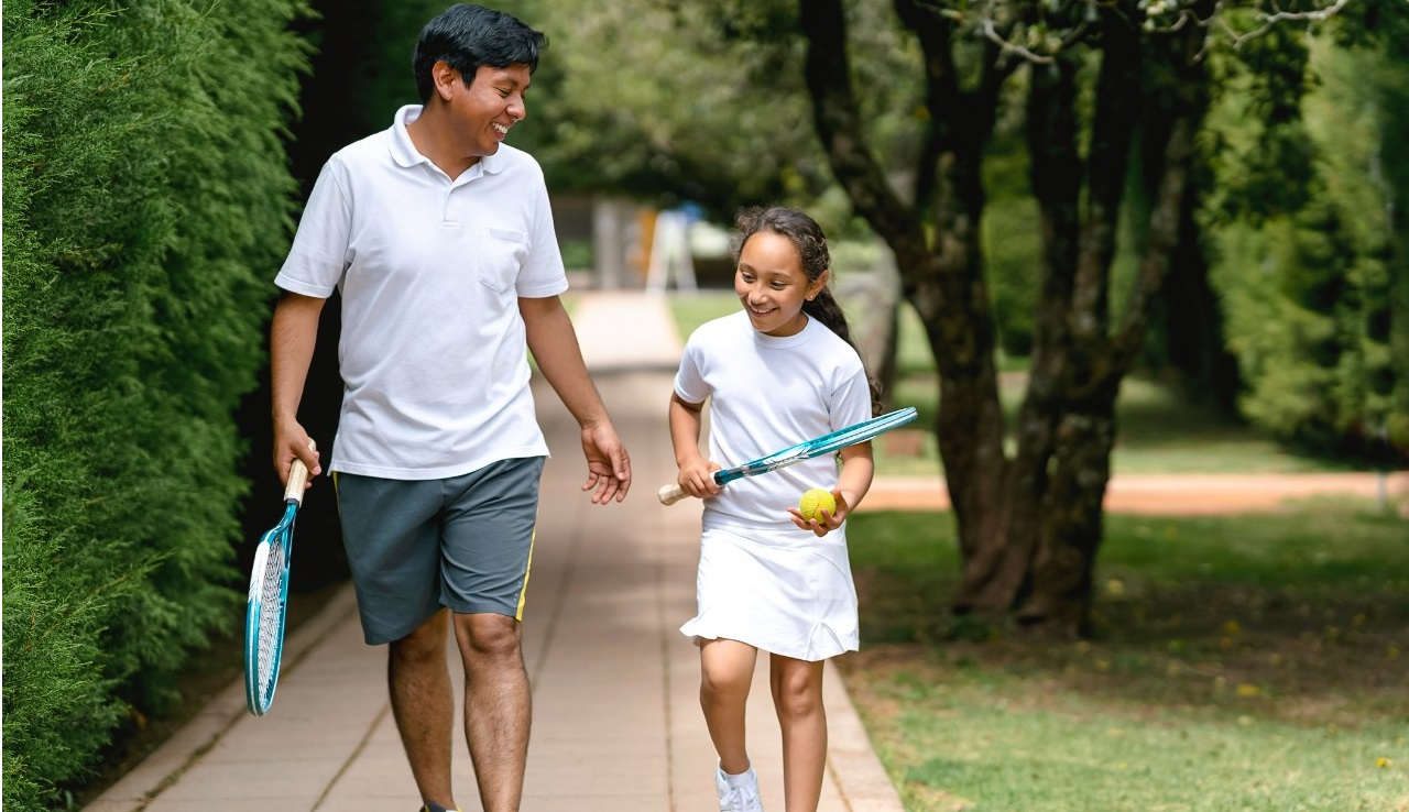 Father and daughter walking to play tennis holding racquets