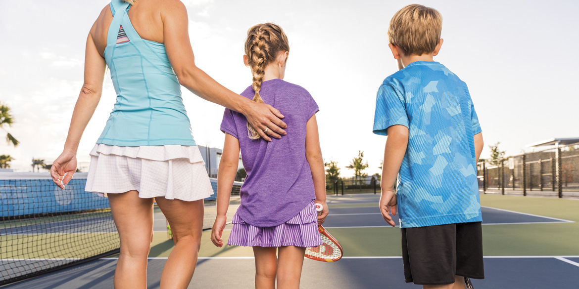 A mother and her two kids walking on a tennis court