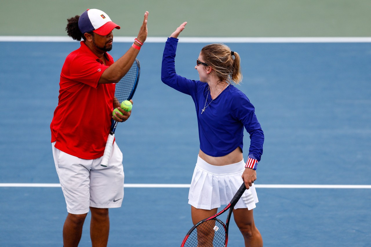 Adaptive tennis players high fiving on the court mid doubles match