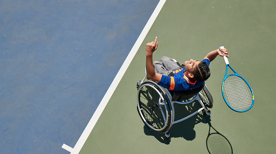 Overhead shot of a wheelchair tennis player cheering on the tennis court, representing the tennis rules for serving after a tiebreak set.