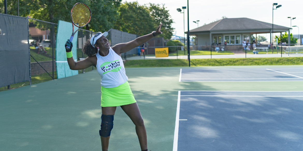 An Adult woman on the tennis court smiling with a white top and neon green skirt on
