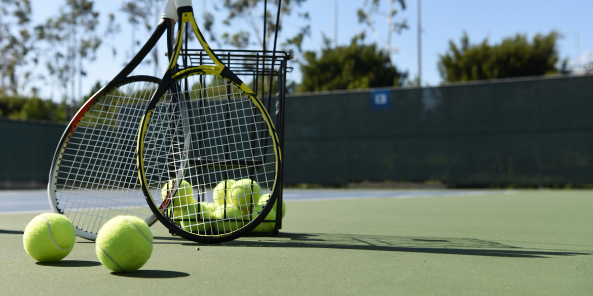 Up close image of tennis balls and a racquet on an outdoor court